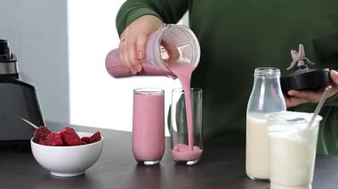 Mutfakta yoğurt ve sütle taze çilekli smoothie hazırlayan yeşil kazaklı bir kadının fotoğrafını çek. Yüksek kaliteli FullHD görüntüler