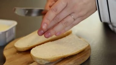 Kadın ellerinin evde bir dilim beyaz ekmeğe yağ sürmesini. Tahta kesme tahtasıyla bulanık bir arkaplan. Yüksek kaliteli FullHD görüntüler