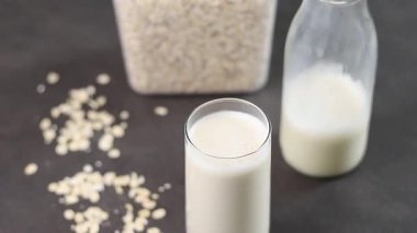 Gri mutfak masasındaki plastik kutuda bir bardak yulaf sütü ve yulaf ezmesi. Vejetaryen ve sütsüz alternatif süt konsepti. Yüksek kaliteli FullHD görüntüler