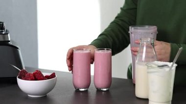 Mutfakta yoğurt ve sütle taze çilekli smoothie hazırlayan yeşil kazaklı bir kadının fotoğrafını çek. Yüksek kaliteli FullHD görüntüler