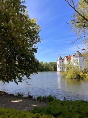 06.06.2025 - Flensburg Almanya. Gölde yüzen beyaz kuğulu tarihi şato, arka planda mavi gökyüzü 