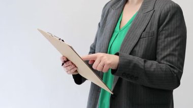 Elinde bir dosya tutan ve onu gösteren gri, boş bir stüdyo arkaplanı olan bir kadının yakın çekimi. Yüksek kaliteli FullHD görüntüler. Yüksek kaliteli FullHD görüntüler