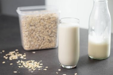 Bir bardak laktozsuz yulaf ezmesi ve yulaf ezmesi gri mutfak masasında, arka planda bulanık. Vejetaryen ve sütsüz alternatif süt kavramı