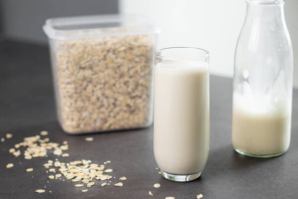 Стакан безлактозного овсяного молока и овсянка в коробке на сером кухонном столе, размытый фон. Концепция веганского и немолочного молока