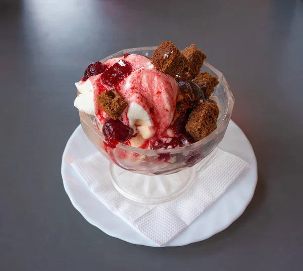 White ice cream with red jam and biscuit in a glass cup close-up