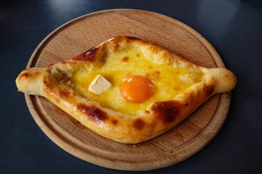 Ahşap bir tahtanın üzerinde Adjarian Khachapuri - geleneksel. Gürcistan mutfağı. Yumurtalı, peynirli ve tereyağlı ekmek