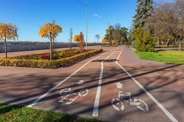 Bicycle path in the city garden along the river embankment on a sunny autumn day. Kremenchuk city, Ukraine.