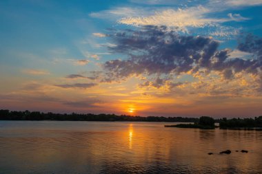 Dinyeper nehrinin üzerinde bulutların olduğu manzaralı bir gün batımı. Yazın Ukrayna doğası
