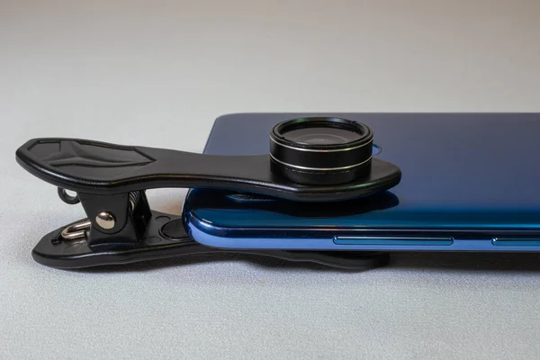 Lens mounted on a phone camera. An additional lens is attached to a blue smartphone camera on a white background. Close-up side view