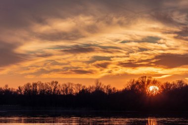 Batan güneşin üzerinde gökyüzünde resim gibi bulutlar, bir nehir ve bir orman ile güzel bir akşam manzarası. HDR fotoğrafı