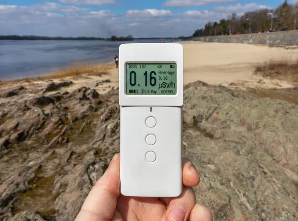 Dosimeter radiometer in hand measures the level of radiation on the beach and stones. Measurement of the dose rate of ionizing radiation in a public place. Environmental pollution control