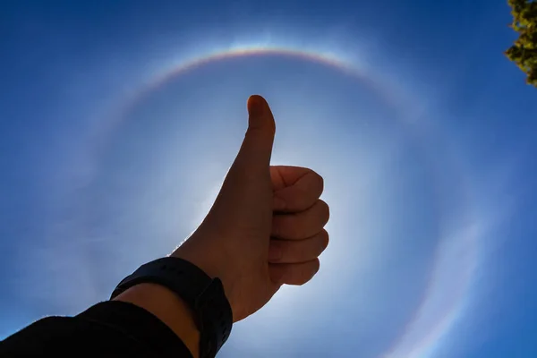 人の手は 大気中の光学現象 で空に対してのように示しています 太陽の周りの虹の円 — ストック写真