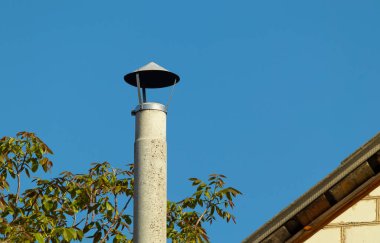 Beton baca borusu evin çatısının kenarı ve dallardaki yapraklar açık mavi gökyüzünün arka planına karşı.