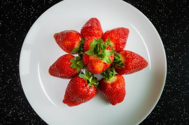 Siyah bir masada beyaz bir tabakta büyük doğal kırmızı çilekler. Büyük böğürtlenler sağlıklı tatlı tatlılardır.