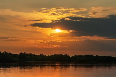 Gün batımında bir nehir ve orman üzerinde güneşi yiyen bir hayvan şeklinde bir bulut. HDR fotoğrafı