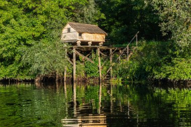Güneşli bir yaz gününde, nehrin kıyısında ya da gölde sütunların üzerinde küçük bir bungalov.