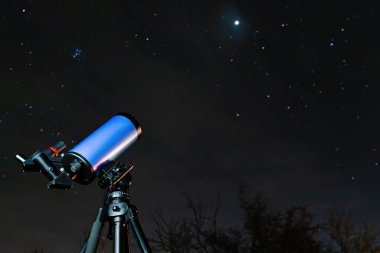 Bir tripodun üzerindeki astronomik bir teleskop geceleri yıldızları seyretmeye hazırdır. Yıldızlı gökyüzü nesnelerini incelemek için modern bir optik aygıt