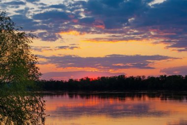 Bir yaz akşamı kırsal kesimde geniş bir nehrin üzerindeki bulutlarla gün batımı manzarası