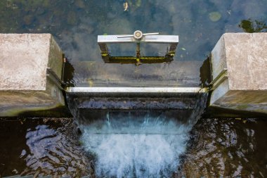 Küçük bir nehirde taşan küçük bir baraj oluğu. Nehirdeki su seviyesini kontrol etmek için şelaleli bir geçit, üst manzara.