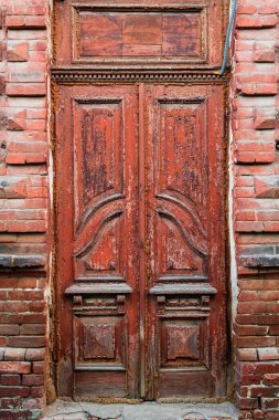 Tuğla evin eski ahşap kapısı. Kırık kırmızı boyalı, kırmızı tuğlalı bir binanın giriş kapısı.