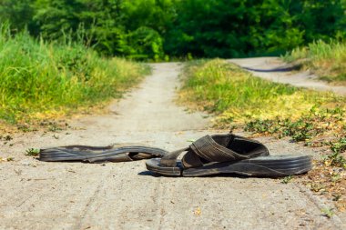 Tozlu bir yolda siyah yırtık terlikler. Köy yolunda terk edilmiş ayakkabılar. Güneşli yaz günü, kimse yok.