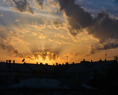 Gökyüzü ve günbatımı bulutlar ve güneş ışınları ile şehirdeki evlerin çatıları üzerinde