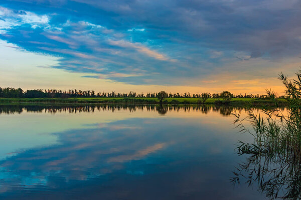 Picturesque landscape with lake and clouds reflection on calm water surface. Countryside nature on summer evening