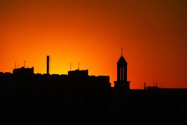 Gökyüzü açık turuncu-kırmızı bir günbatımına karşı binaların siluetleri ve bir cami. Kharkiv şehri, Ukrayna