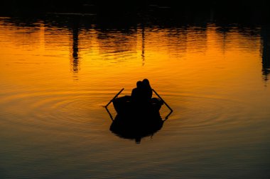 Gün batımında suda kayıkla gezen çiftlerin silueti. Romantik bir buluşma ve dışarı çıkmak.