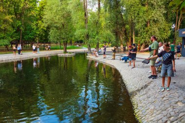 Kharkiv şehri, Ukrayna - 28 Ağustos 2024: Sarzhin Yar şehir parkındaki gölette amatör balıkçılık. Erkekler, kadınlar ve çocuklar çubuklarla balık yakalar. Sarzhynka nehri üzerindeki dekoratif gölet.