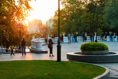 Kharkiv şehri, Ukrayna - 10 Ekim 2024: Şehir parkı insanların gün batımında akşam manzarasının keyfini çıkardıkları bir yer. İnsanlar korkulukta durup manzaranın tadını çıkarıyorlar. Ağaçların dallarında sıcak güneş ışığı