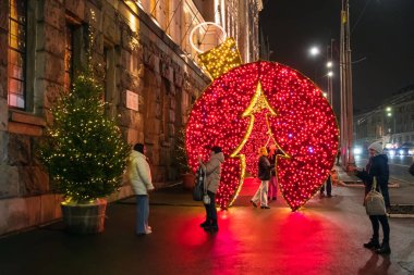 Kharkiv şehri, Ukrayna - 09 Aralık 2024: Genç kadınlar yeni yıl ağacı yakınında fotoğraf çekiyorlar ve kaldırımda tesisleri aydınlatıyorlar. Açık havada aydınlatılmış Noel süslemeleri