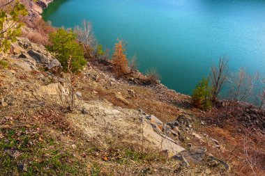 Suyun yanındaki kayalık yamaçta. Terk edilmiş bir taş ocağının dibindeki bir gölün kıyısında.