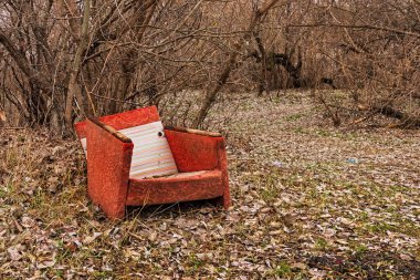 Old broken armchair in the forest. Abandoned furniture outdoors. Red Lounge chair