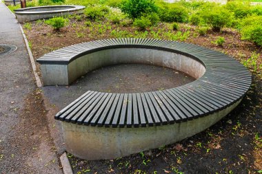 Asfalt yolunun yakınındaki park bankında. Ahşap tahtalar ve beton tabanlı dairesel bank