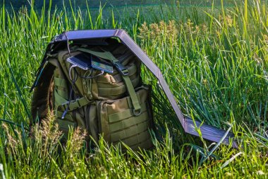 Güneş paneli yeşil çimlerin üzerinde sırt çantasının üzerinde katlanıyor. Akıllı telefonlar ve kişisel elektronik cihazlar için taşınabilir güneş enerjisi şarj istasyonu