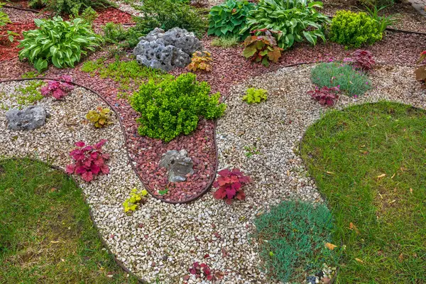 Çeşit çeşit bitki ve çalılarla dolu bir çiçek tarlası, çakıl taşları. Güzel, modern bahçe tasarımı, küçük taş gübreli.