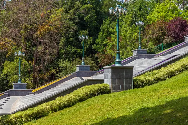 Güneşli bir yaz gününde parkta ya da şehir bahçesinde bir sütunda büyük taş merdiven. Eski tarz güzel sokak lambaları.