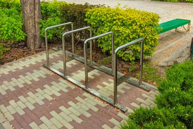 Açık havada bisiklet parkı. Çalıların yanındaki parkta bisiklet rafı. Krom borulardan yapılmış demir yapı.