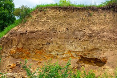 Kumlu ve çamurlu toprağın dik bir bölümü kuş yuvası gibidir. Farklı renklerde çamur katmanları. Kharkiv bölgesi, Ukrayna. Sarı ve turuncu toprak