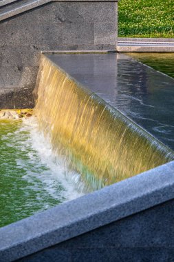 Parktaki şelalede taş ve granit levhalarla çerçevelenmiş yapay dekoratif göletler var. Akan su dökülür ve köpük olur.