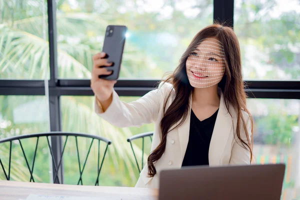 Businesswoman using smartphone to scan face for identity verification to unlock in digital connection access to financial transaction data, facial recognition technology, data protection.