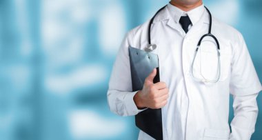 Beyaz önlüklü bir doktor elinde bir pano ve steteskop ile klinik bir ortama güveni yansıtıyor, sağlık ve hasta güvenini vurguluyor..