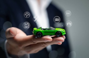 Bir el, dijital simgelerle çevrili, otomotiv endüstrisindeki yenilik ve teknolojiyi sembolize eden canlı yeşil oyuncak bir araba sunuyor. İş temaları için mükemmel.