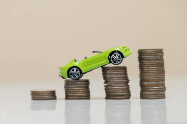Canlı yeşil bir oyuncak araba madeni para yığınlarının üzerinde dengede duruyor ve mali büyüme ve yatırım stratejilerini sembolize ediyor. Mali temalar için ideal.