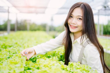 Genç bir kadın serada taze marullarla ilgilenirken ışıl ışıl gülümser. Bu canlı sahne, bahçıvanlığın ve doğanın güzelliğini yansıtıyor..