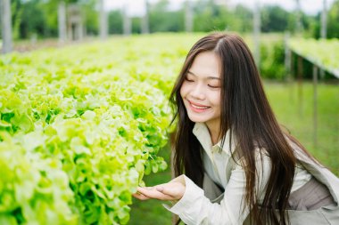 Neşeli bir kadın canlı yeşil marul ile etkileşim içinde bahçe ortamında, doğanın güzelliğini ve sağlıklı yaşamı kutluyor. Güneş ışığı sahnenin tazeliğini arttırır.