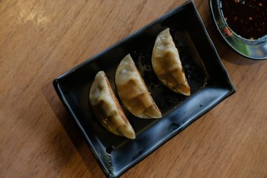 Kırmızı soya sosuyla servis edilen siyah seramik tabakta 3 parça ızgara gyoza.