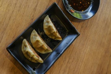 Kırmızı soya sosuyla servis edilen siyah seramik tabakta 3 parça ızgara gyoza.