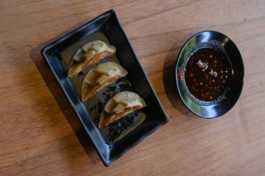 Kırmızı soya sosuyla servis edilen siyah seramik tabakta 3 parça ızgara gyoza.